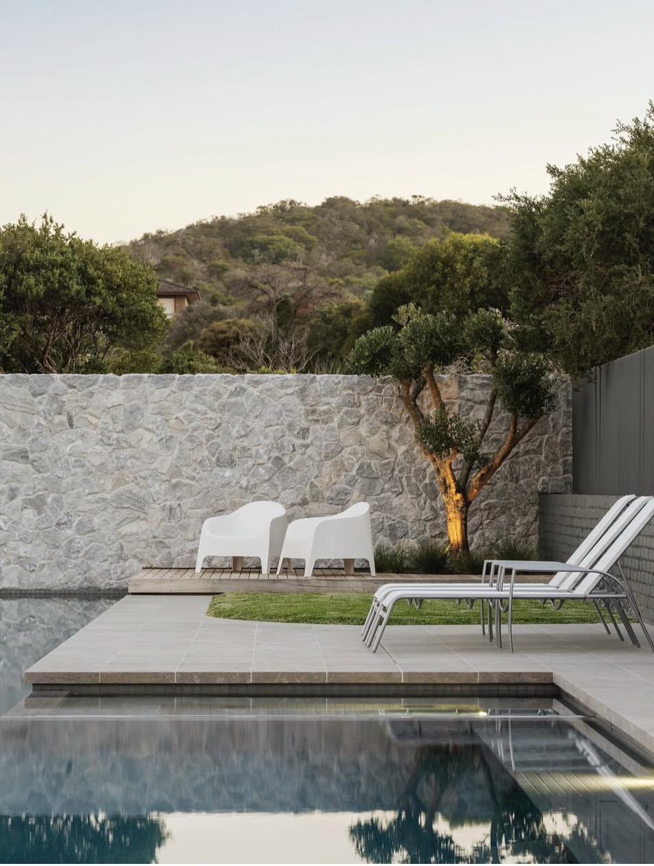 Uplit cloud-pruned olive tree against a stone wall beside a pool, Portsea project for COS Design
